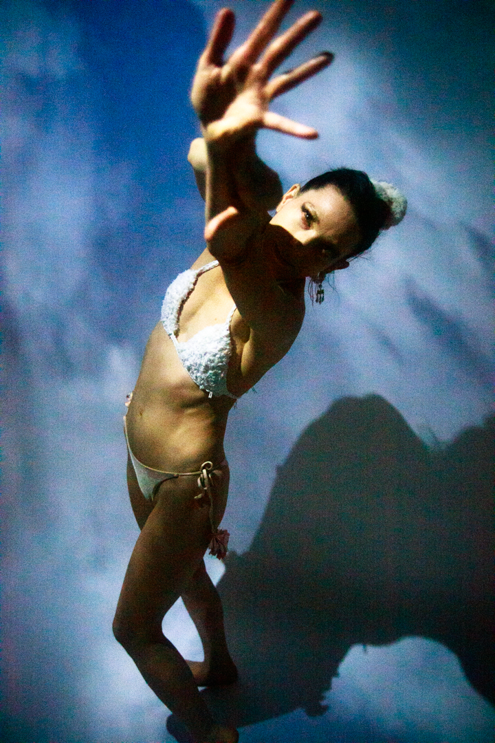 A women in a bikini standing in the sky, with her hands overhead.