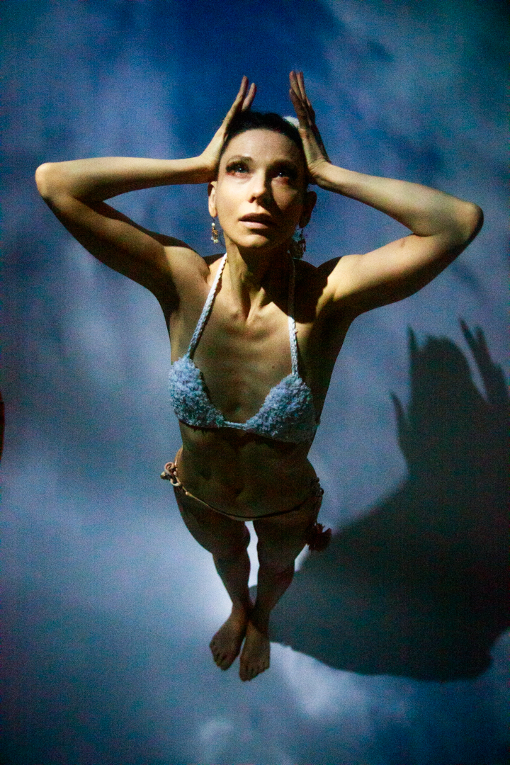 A women in a bikini standing in the sky, with her hands on her head.