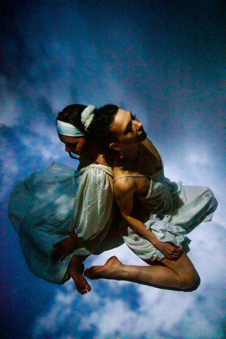 Two women sitting in the sky back to back.
